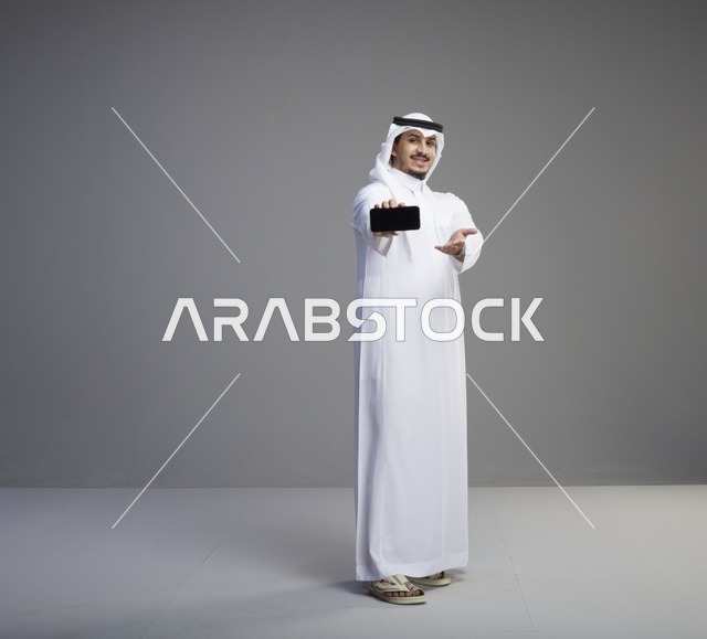 رجل سعودي يمسك هاتف ذكي بشاشة فارغة في الاستوديو