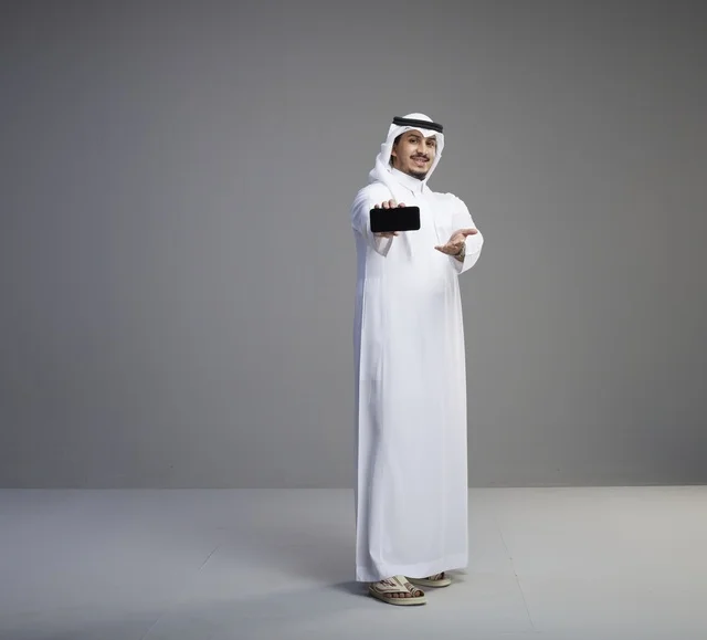 رجل سعودي يمسك هاتف ذكي بشاشة فارغة في الاستوديو