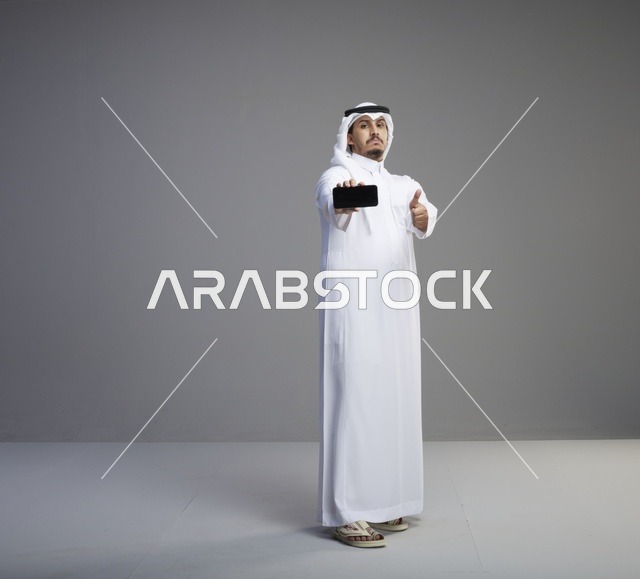 رجل سعودي يحمل هاتف ذكي بشاشة فارغة مع إشارة الإعجاب