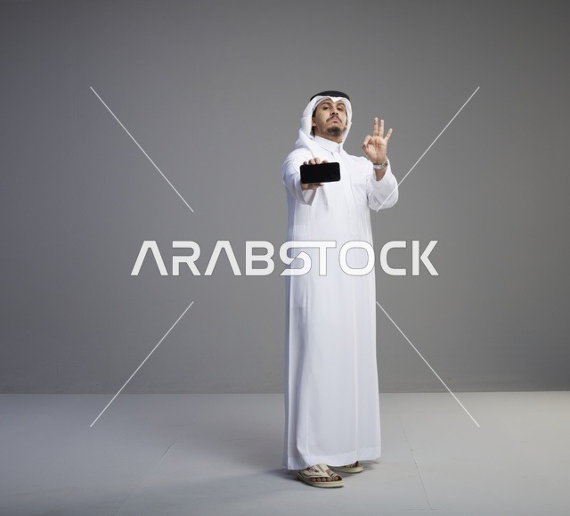 رجل سعودي يحمل هاتف ذكي بشاشة فارغة مع علامة تمام