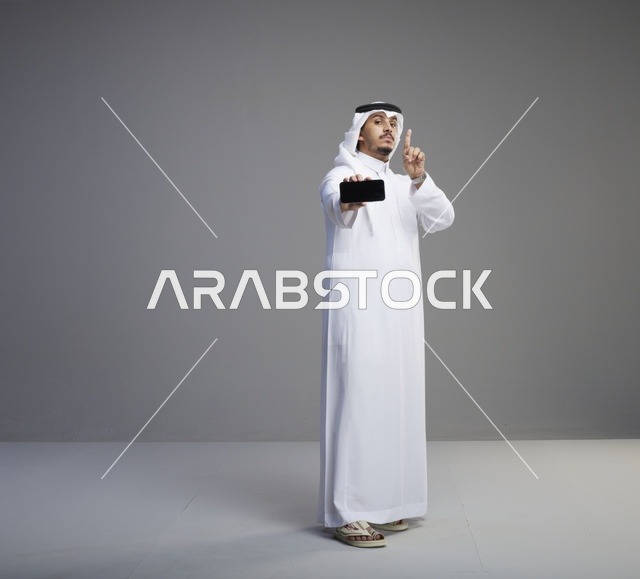 رجل سعودي يحمل هاتف ذكي بشاشة فارغة في استوديو