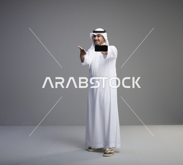 رجل سعودي يحمل هاتف ذكي بشاشة فارغة في استوديو