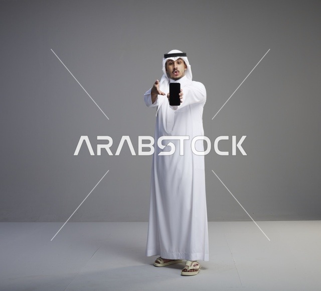رجل سعودي يحمل هاتفاً ذكياً بشاشة فارغة في الاستوديو