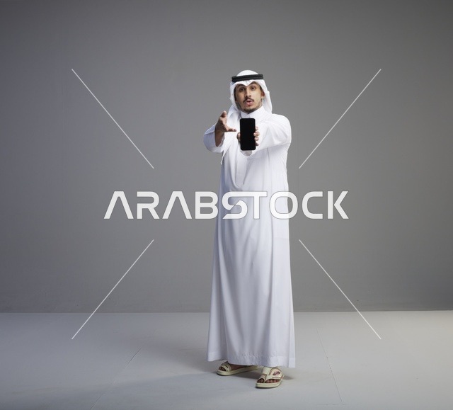 رجل سعودي يحمل هاتف ذكي بشاشة فارغة في استوديو