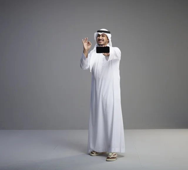 رجل سعودي يحمل هاتف ذكي بشاشة فارغة في استوديو