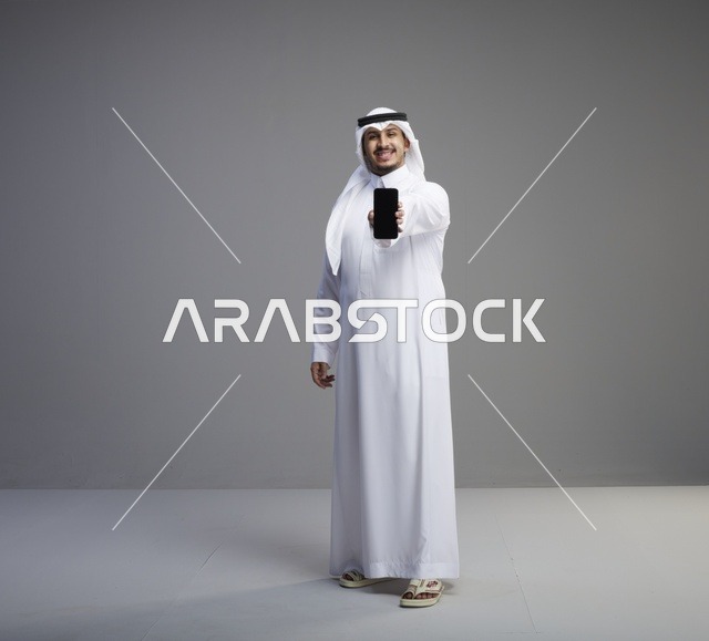 رجل سعودي يمسك هاتف ذكي بشاشة فارغة في الاستوديو