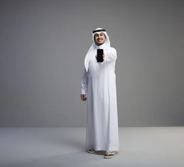 رجل سعودي يمسك هاتف ذكي بشاشة فارغة في الاستوديو