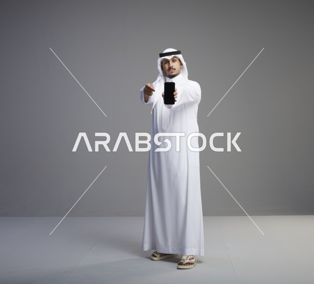 رجل سعودي يحمل هاتف ذكي بشاشة فارغة في استوديو