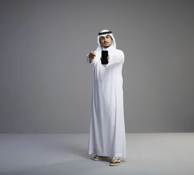 رجل سعودي يحمل هاتف ذكي بشاشة فارغة في استوديو