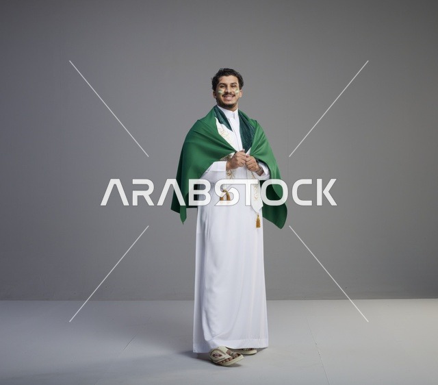 شاب سعودي يلتف بعلم المملكة بالثوب التقليدي