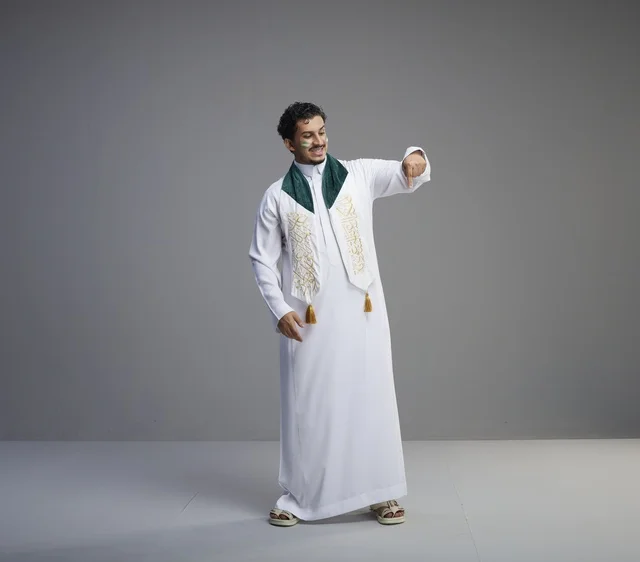 شاب سعودي بالزي التقليدي يشير للأسفل في احتفال وطني