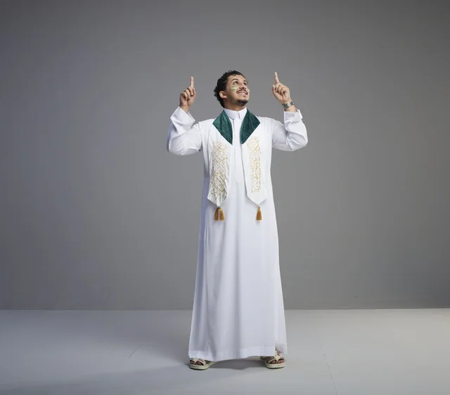 شاب سعودي بملابس اليوم الوطني يشير للأعلى