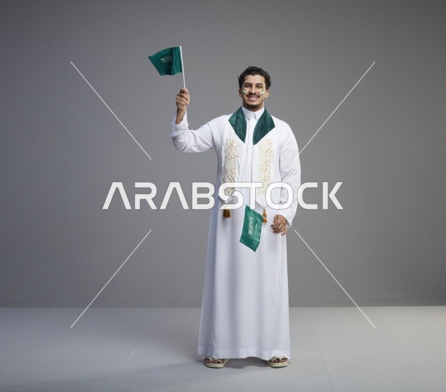 شاب سعودي بالثوب التقليدي يحمل أعلام المملكة