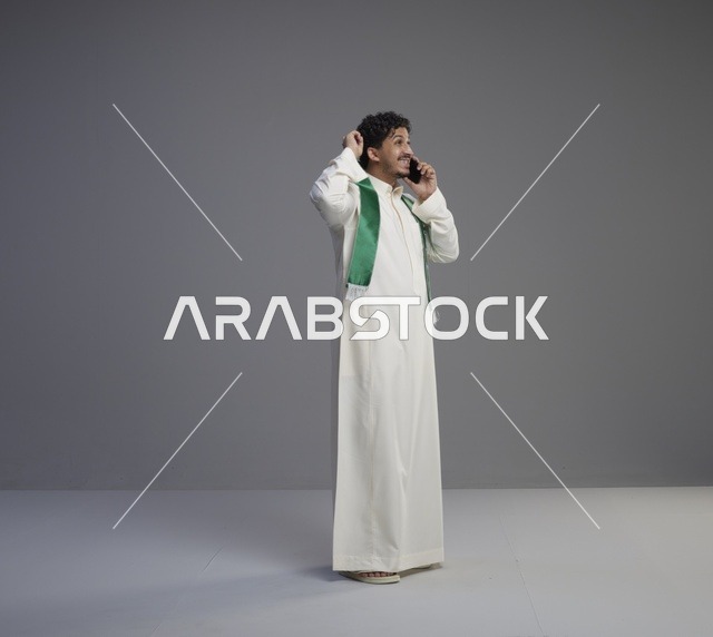 شاب سعودي بالثوب والوشاح الأخضر يتحدث بالهاتف الذكي