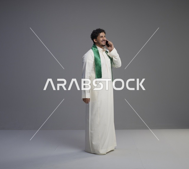 شاب سعودي يتحدث عبر الهاتف بالثوب والوشاح الأخضر