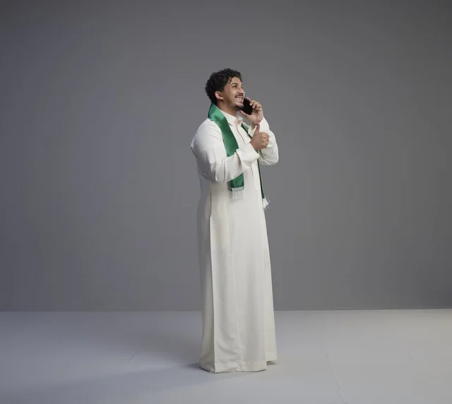 شاب سعودي يتحدث بالهاتف مع وشاح اليوم الوطني