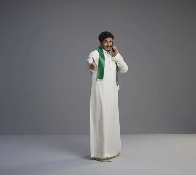 شاب سعودي بالثوب يتحدث بالجوال ويمد يده للمصافحة