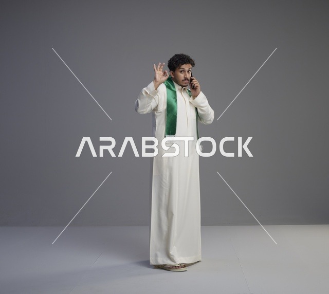 شاب سعودي يتحدث عبر الجوال بوشاح اليوم الوطني