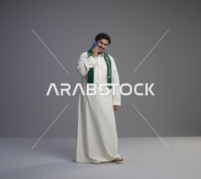 شاب سعودي يتحدث عبر الهاتف بالثوب والوشاح الأخضر