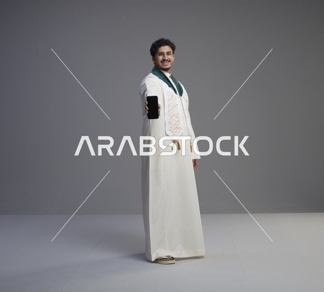 شاب سعودي بالثوب التقليدي يحمل هاتف ذكي