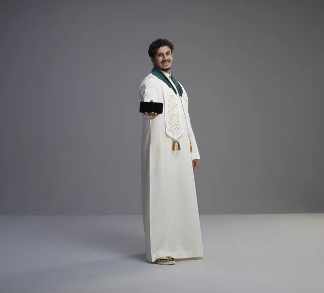شاب سعودي بالثوب التقليدي يحمل شاشة هاتف ذكي
