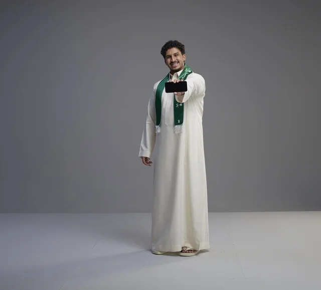 شاب سعودي يحمل هاتف ذكي بشاشة فارغة