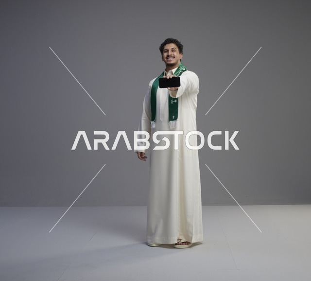 شاب سعودي يحمل شاشة هاتف ذكي في الاستوديو