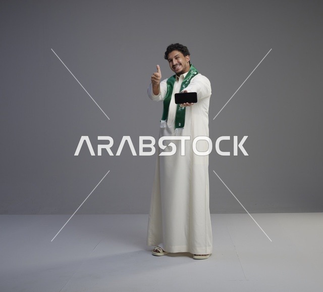 شاب سعودي يحمل هاتف ذكي مع إشارة الإعجاب
