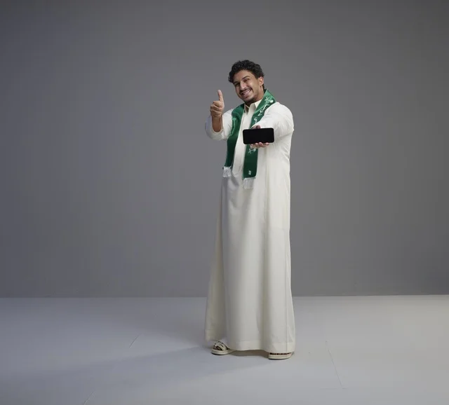 شاب سعودي يحمل هاتف ذكي مع إشارة الإعجاب