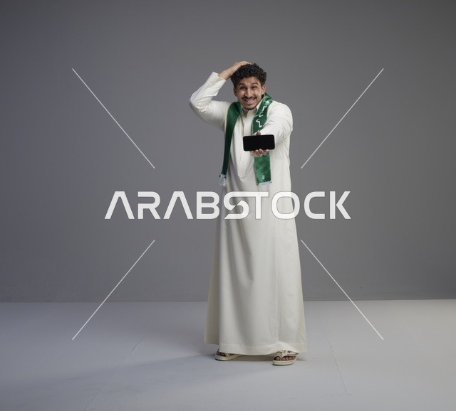 شاب سعودي يحمل هاتف ذكي بتعبير وجه مندهش