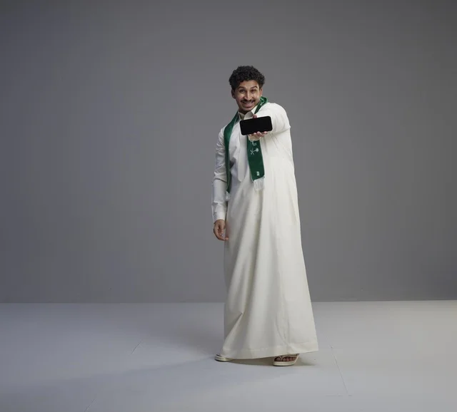 شاب سعودي يحمل هاتف ذكي بشاشة فارغة