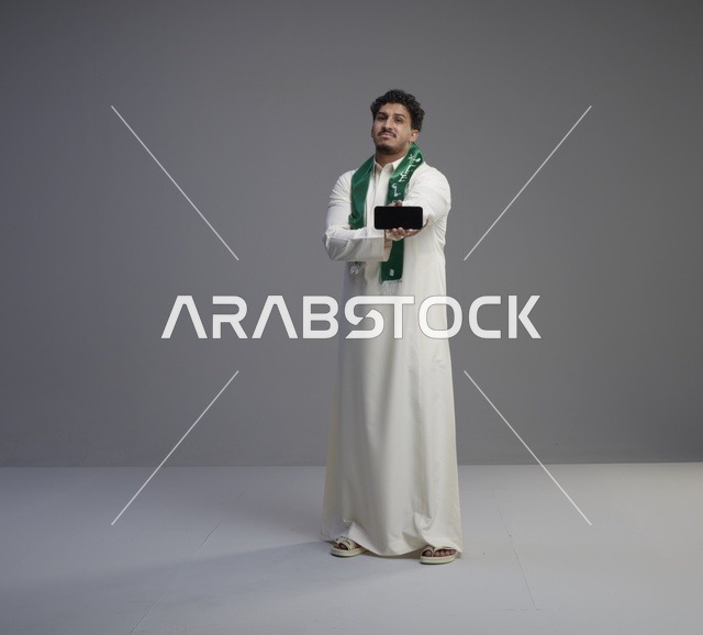 شاب سعودي يحمل هاتف ذكي بشاشة فارغة في الاستوديو
