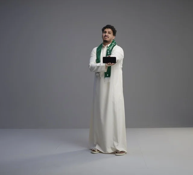 شاب سعودي يحمل هاتف ذكي بشاشة فارغة في الاستوديو