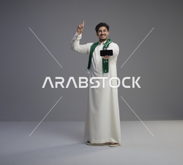 شاب سعودي يحمل هاتف ذكي ويشير للأعلى