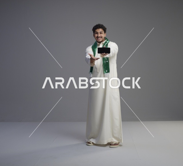شاب سعودي يحمل هاتفاً ذكياً في اليوم الوطني للمملكة