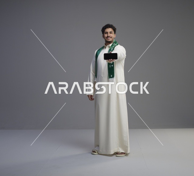 شاب سعودي يحمل هاتف ذكي بشاشة فارغة في استوديو