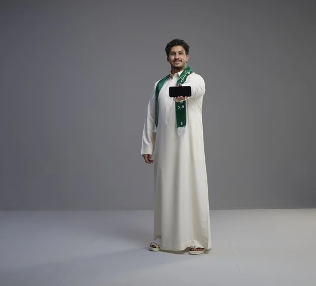 شاب سعودي يحمل هاتف ذكي بشاشة فارغة في استوديو