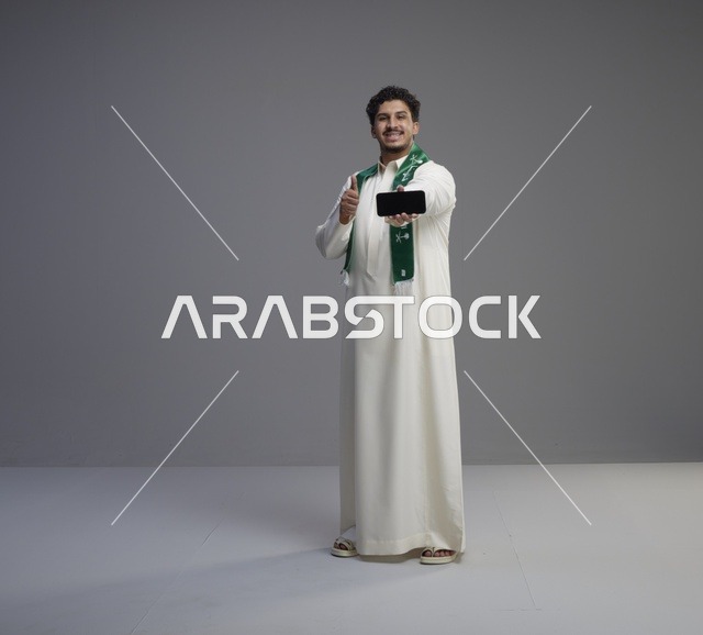 شاب سعودي يحمل هاتف ذكي مع إيماءة الإعجاب