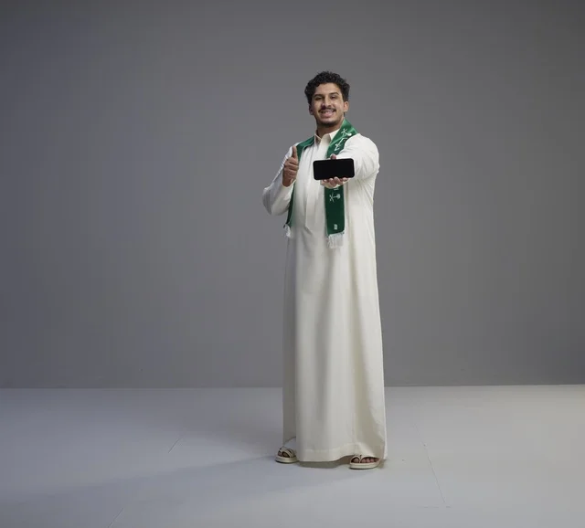 شاب سعودي يحمل هاتف ذكي مع إيماءة الإعجاب