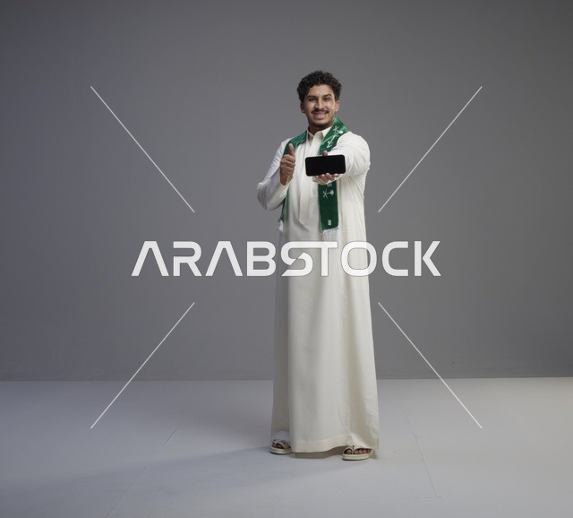 شاب سعودي يحمل هاتف ذكي مع إيماءة الإبهام