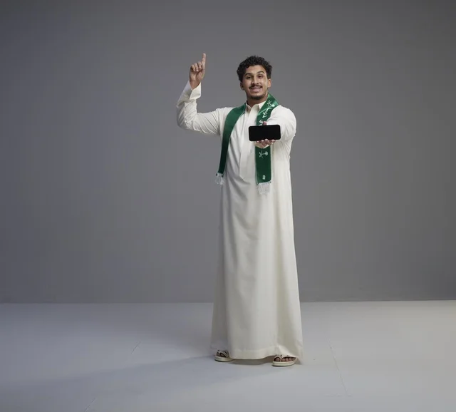 شاب سعودي يحمل هاتف ذكي ويشير للأعلى في استوديو