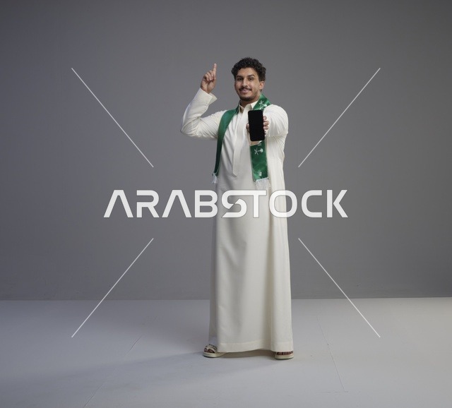 شاب سعودي يحمل هاتف ذكي ويشير للأعلى في استوديو