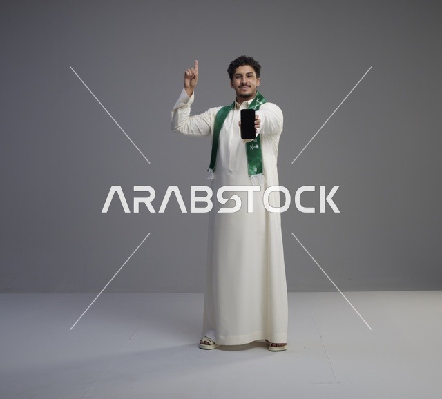 شاب سعودي يحمل هاتف ذكي ويشير للأعلى