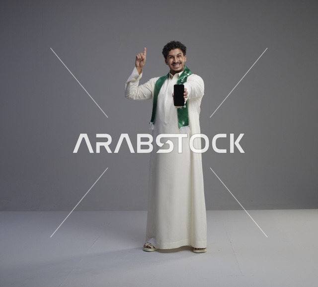 شاب سعودي بالثوب التقليدي يعرض شاشة الجوال