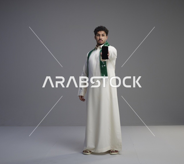 شاب سعودي يحمل هاتف ذكي بشاشة فارغة في الاستوديو