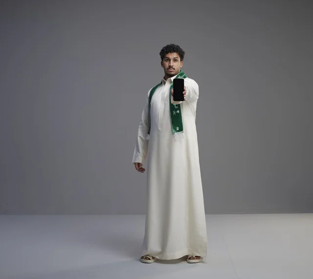 شاب سعودي يحمل هاتف ذكي بشاشة فارغة في الاستوديو