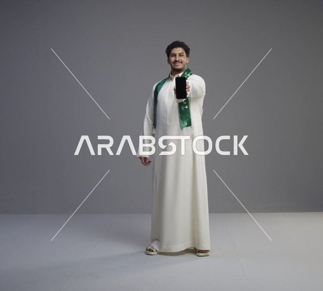 شاب سعودي يمسك هاتف ذكي بشاشة فارغة في استوديو