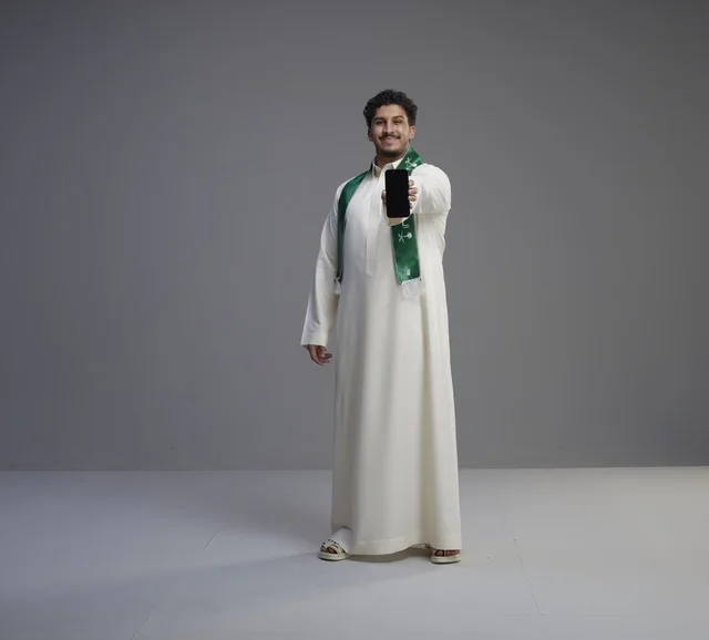 شاب سعودي يمسك هاتف ذكي بشاشة فارغة في استوديو