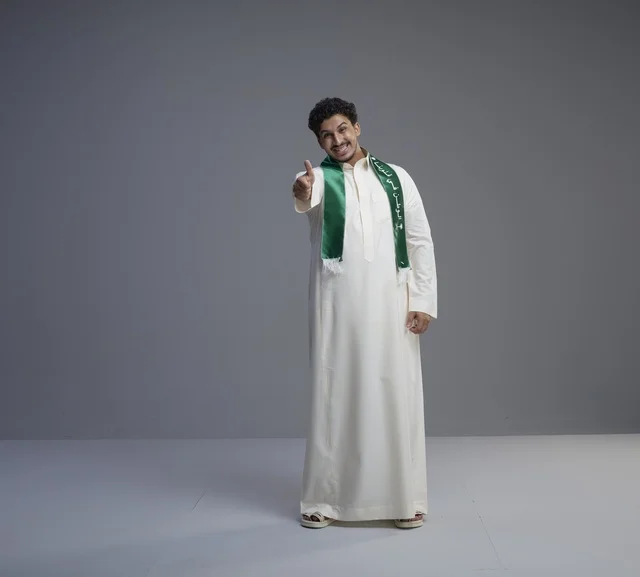 شاب سعودي بوشاح وطني يشير بعلامة الإعجاب