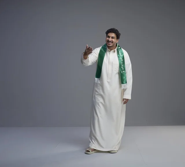 شاب سعودي يرتدي وشاحاً وطنياً أخضر في استوديو